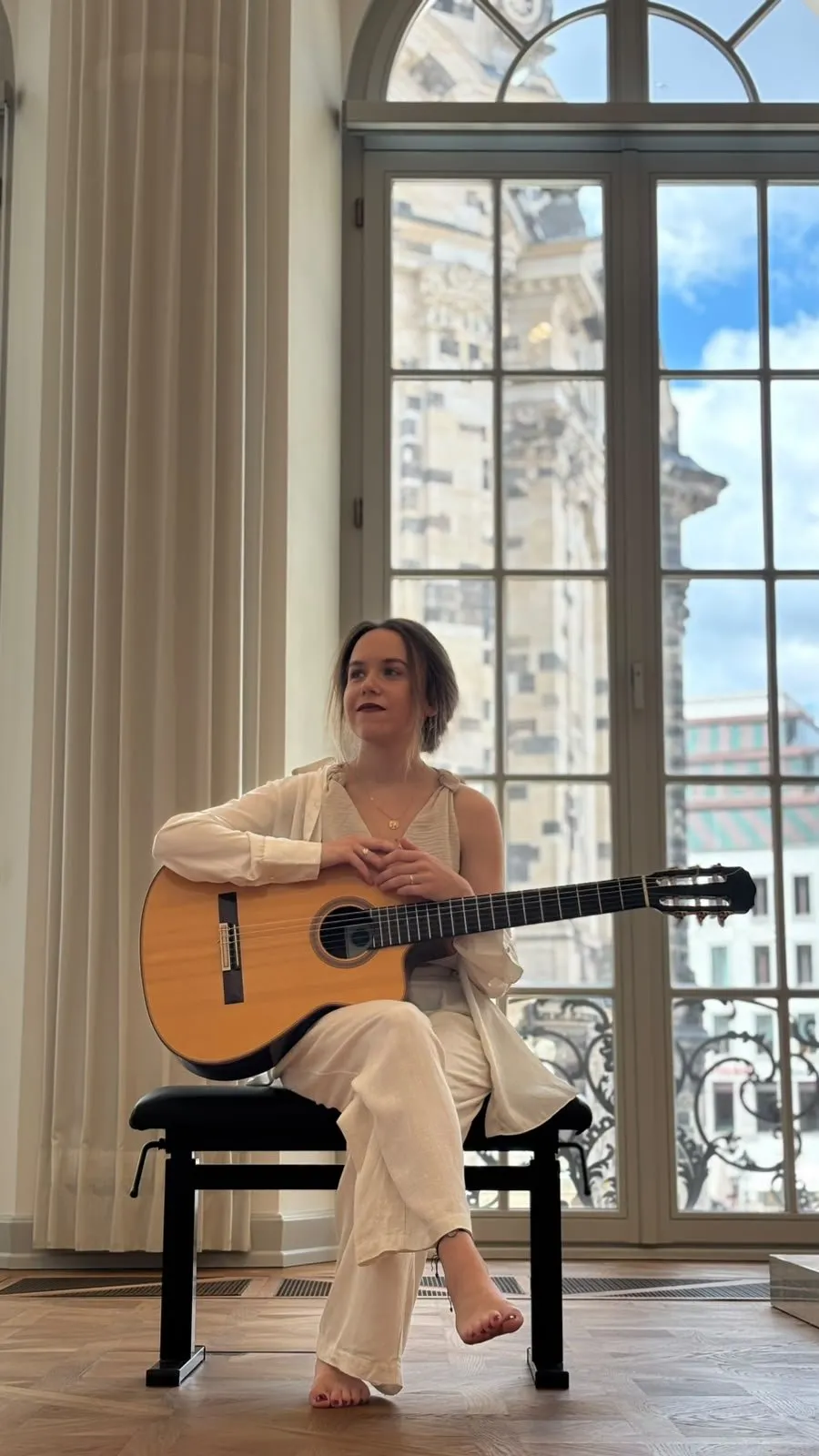 Margaréta Lakner seated with her guitar at a window overlooking Dresden