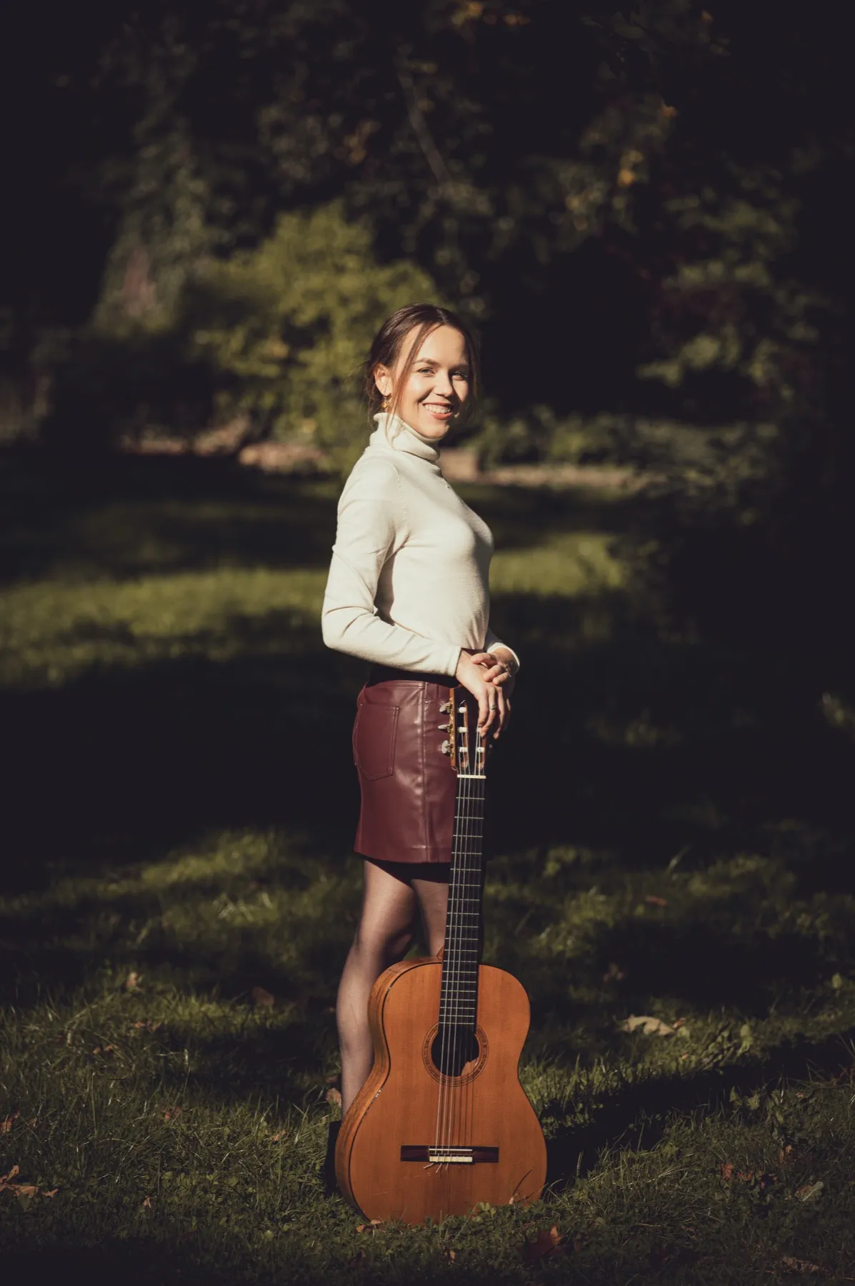 Margaréta Lakner standing with her classical guitar in an autumn park