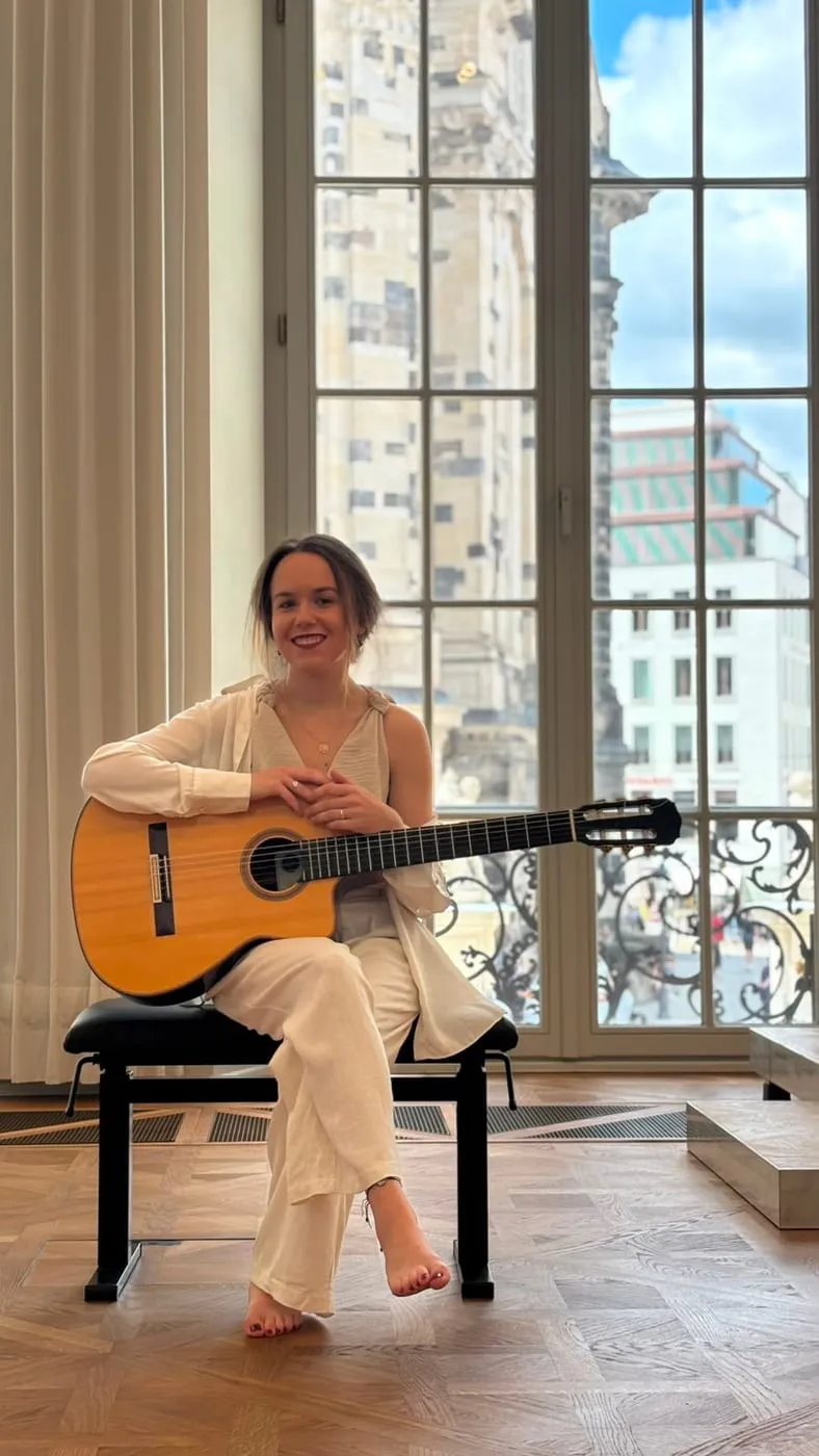 Margaréta Lakner playing guitar beside a tall window